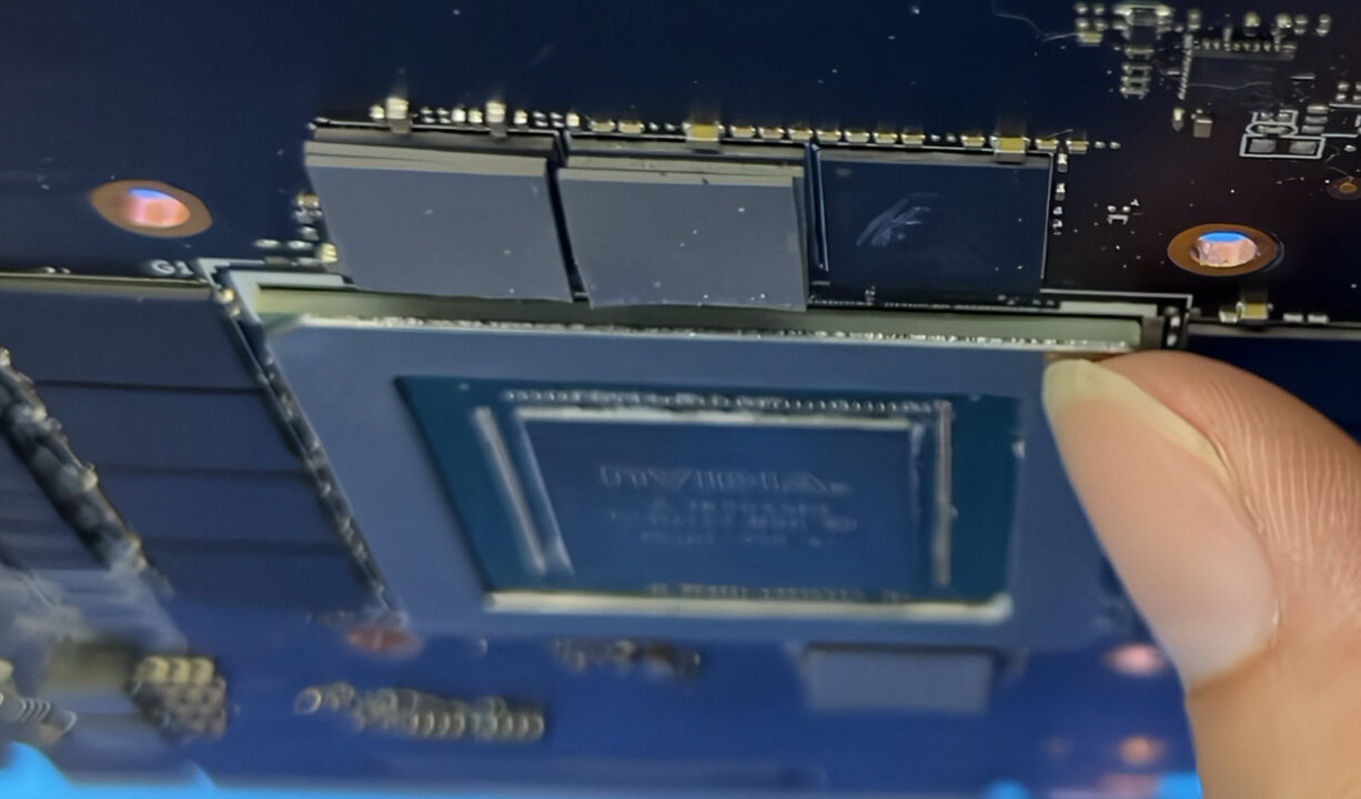 1000041531 Close-up of a graphics card with a memory module being inserted; a finger holds the edge of the module.