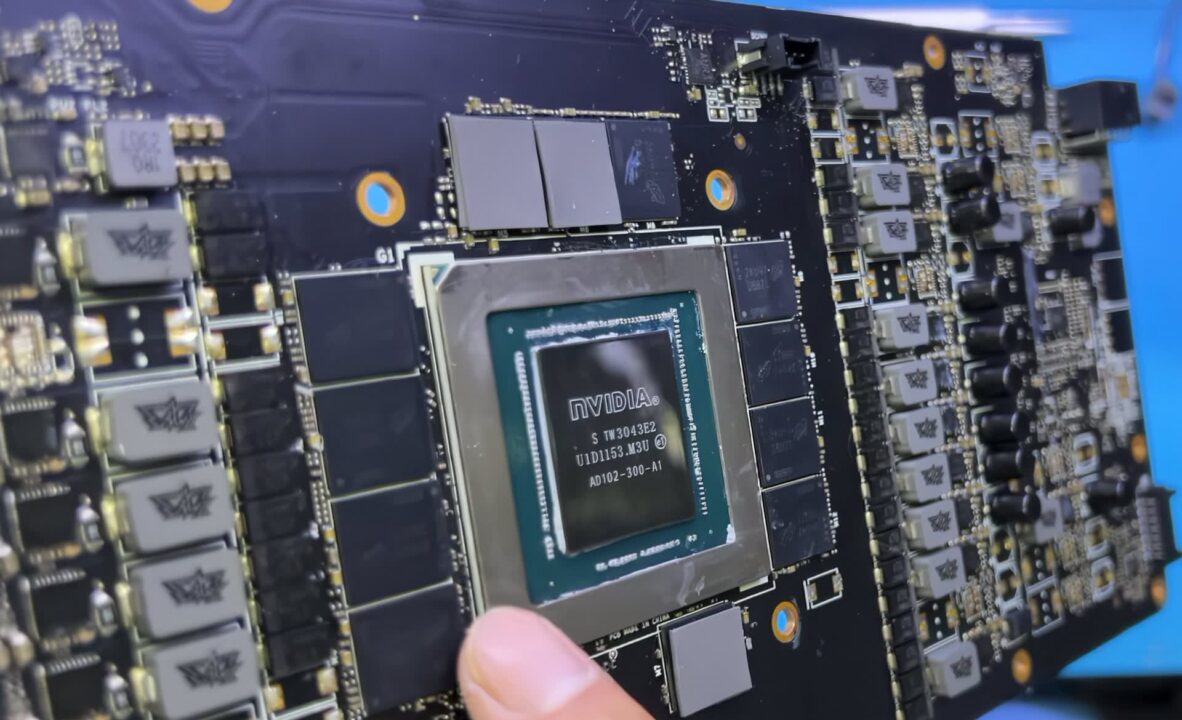 1000041532 Close-up of an Nvidia GPU die on a graphics card, held by a finger with surrounding circuit components.