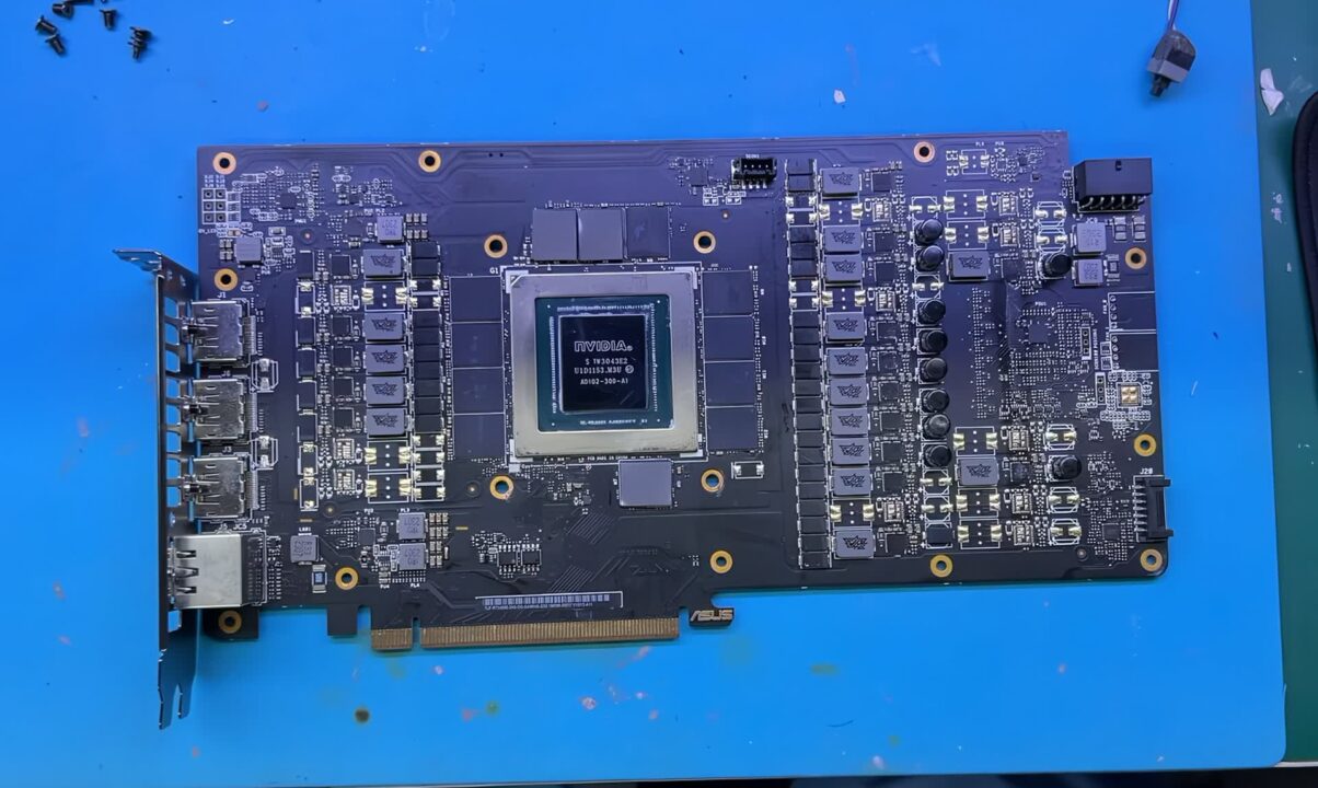 1000041533 Graphics card PCB with an NVIDIA GPU die at the center, PCIe edge at the bottom, and surrounding components on a blue work surface.